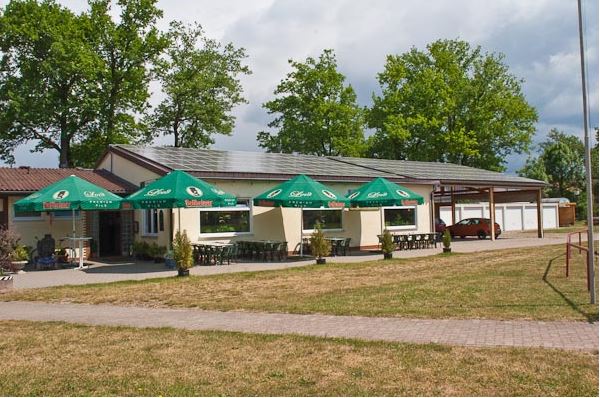 Außenansicht des Schwiegermutters Clubhauses mit grünen Sonnenschirmen und Außensitzplätzen